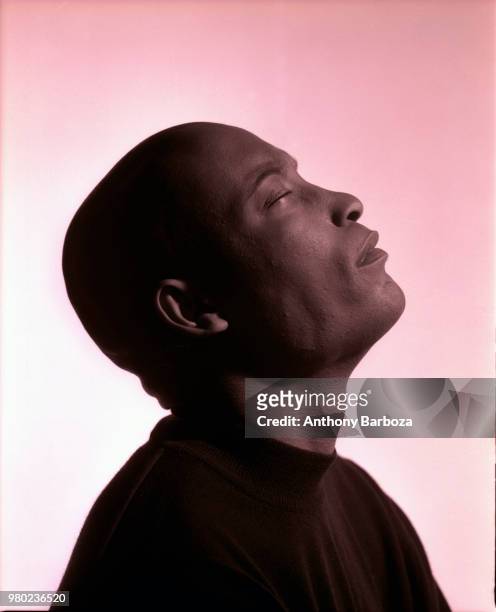 Profile of American film director John Singleton as he poses, with his eyes closed and head tilted back, against a rose-colored background, Los...