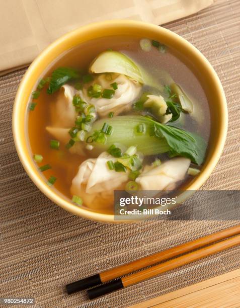 a bowl of shrimp and pork wonton soup in a clear broth with bok choy and chives - napkin and chopsticks - bok choy stockfoto's en -beelden