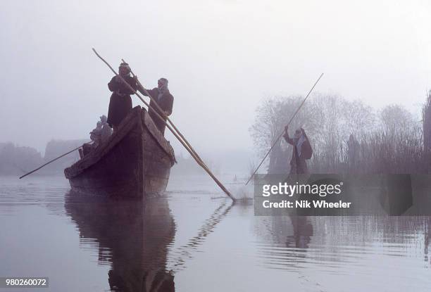 Marsh Arabs steer wooden boats along channel past Marsh Arab village of reed houses in the wetlands of Southern Iraq formed by Tigris and Euphrates...
