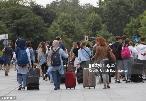 In the city center of Berlin - a large group of young tourists with rolling suitcases and other luggage, photographed from behind.