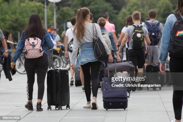 In the city center of Berlin - a large group of young tourists with rolling suitcases and other luggage, photographed from behind.