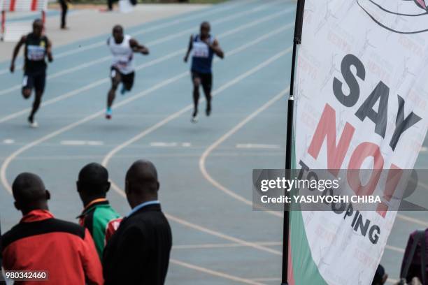 Athletes run as an anti doping banner is seen during the heat of the men's 100m at the Kenya National Trials at Kasarani Stadium in Nairobi on June...