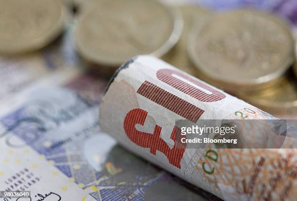Ten pound note and pound coins sit arranged for a photograph in London, U.K., on Thursday, March 25, 2010. The pound had its biggest gain in more...