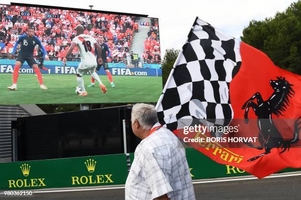 Fan holding a flag with a Ferrari logo watches the Russia 2018 World Cup football match between France and Peru on a large screen at the Circuit Paul...