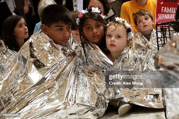 Children wrap themselves up with Mylar blankets to 'symbolically represent the thousands of children separated from families on the border, sleeping...