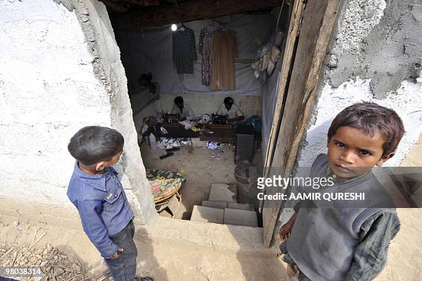 Pakistani tailors stitch up women's dresses as children stand at the shop entrance in a slum area of Islamabad on March 22, 2010. Seventeen million...