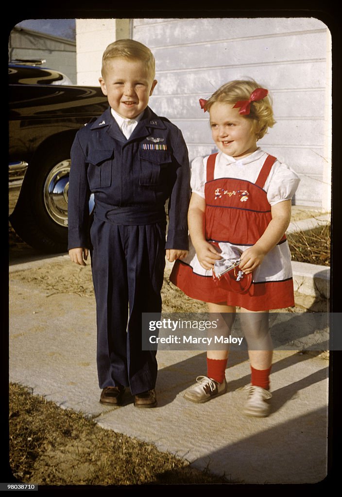 1950's toddlers happily pose in front of Dad's car