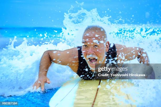 surfer paddling with surfboard on japanese beach in splash. - surfboard fotografías e imágenes de stock