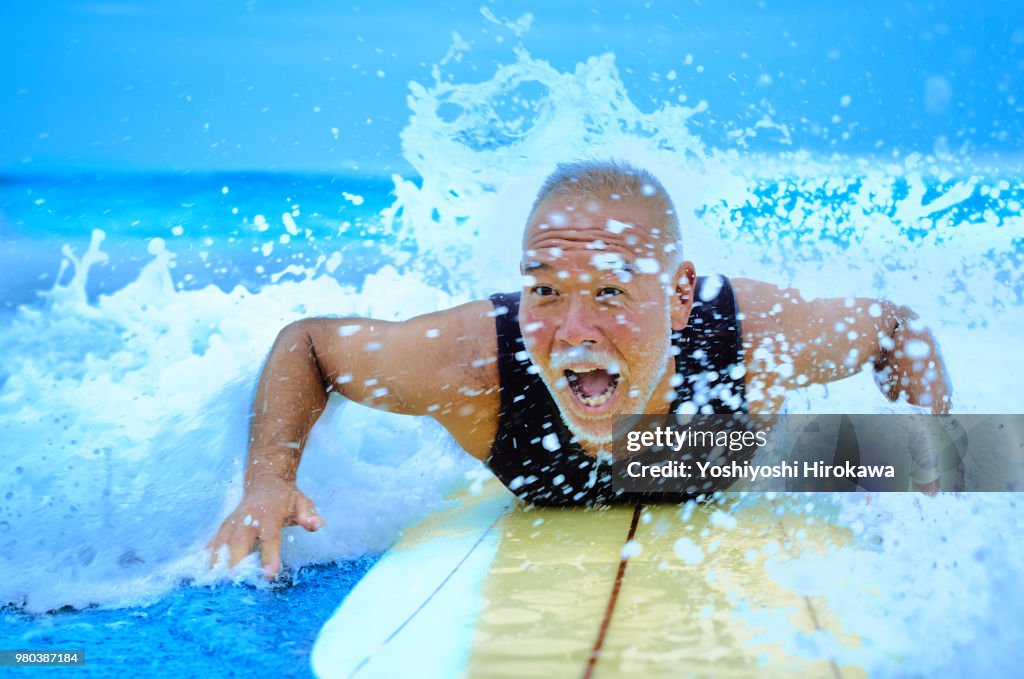 Surfer paddling with surfboard on Japanese beach in splash.