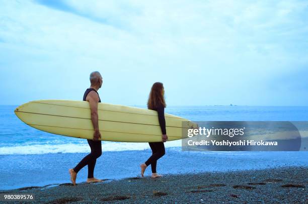 senior couple surfing early in the morning with surfboard - japanese couple beach stock-fotos und bilder