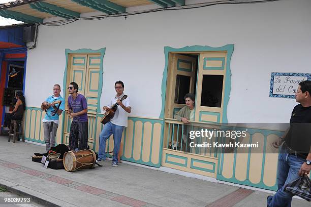 Woman stands behind the door of a coloorful house on the main street where a band is playing music during Salento festival. Salento is a small town...