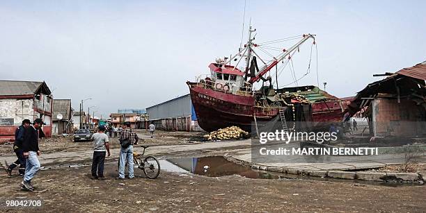 People walk past a fishing boat that was washed ashore in the recent earthquake and tsunami in Talcahuano on March 23 after the February 27th...