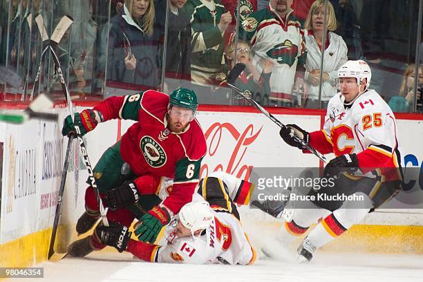 Greg Zanon of the Minnesota Wild collides with Ian White and David Moss of the Calgary Flames while skating to a loose puck during the game at the...