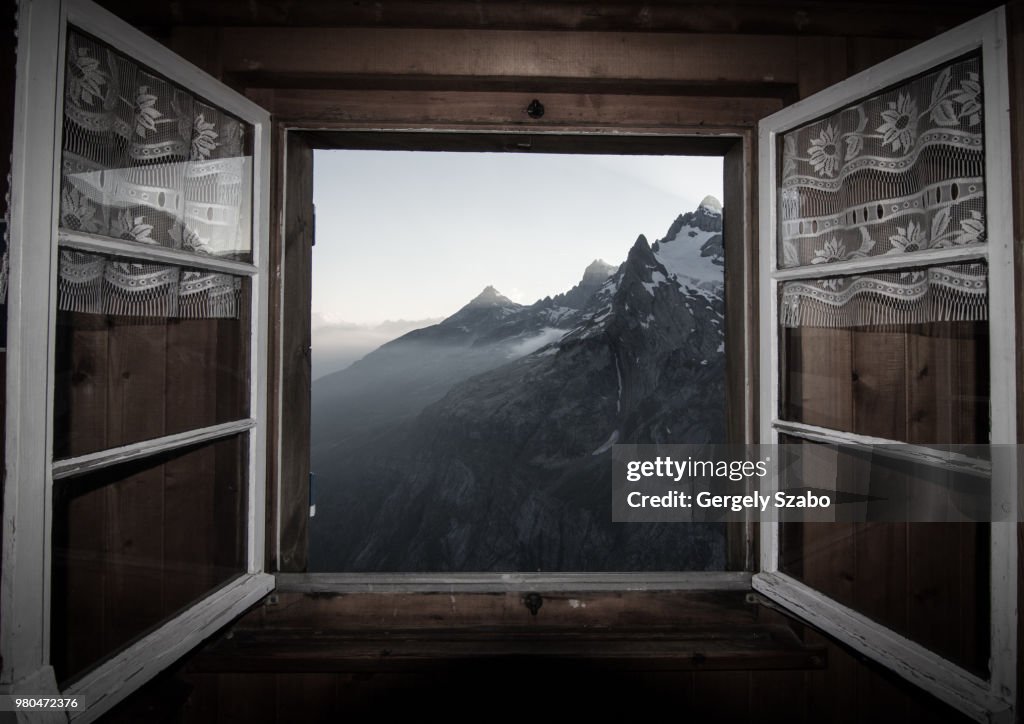 View of the Swiss Alps through a log cabin window in Switzerland.