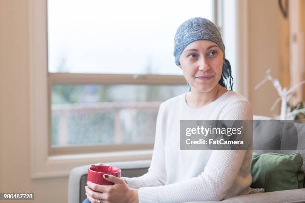 a middle-aged cancer survivor sits by the window and reflects on her life - tomada de decisão imagens e fotografias de stock