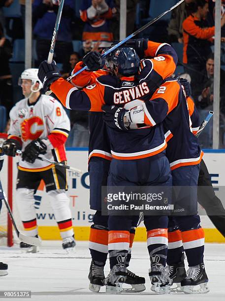 Cory Sarich of the Calgary Flames skates away in the background as teammates congratulate Bruno Gervais of the New York Islanders who just scored the...