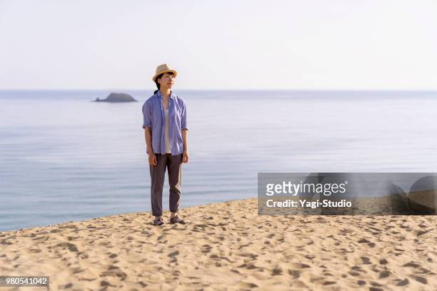 um viajante de mulher relaxar nas dunas de areia atrás do mar - tottori prefecture - fotografias e filmes do acervo