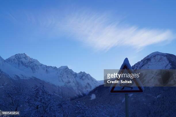 slippery road sign against mountain landscape - señal de pavimento deslizante fotografías e imágenes de stock