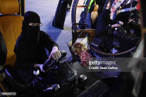 Young woman who is wearing a traditional Muslim niqab tries out a car driving simulator as her child sleeps in a pram parked next to her during an...