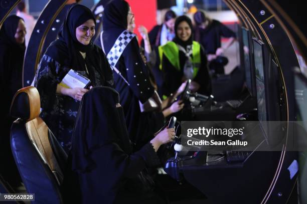 Woman who is wearing a traditional Muslim niqab tries out a car driving simulator as her child sleeps in a pram parked next to her during an outdoor...