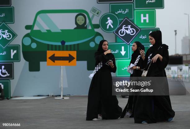 Young women wearing the traditional abaya walk past a sign as they help to organize an outdoor educational driving event for women on June 21, 2018...