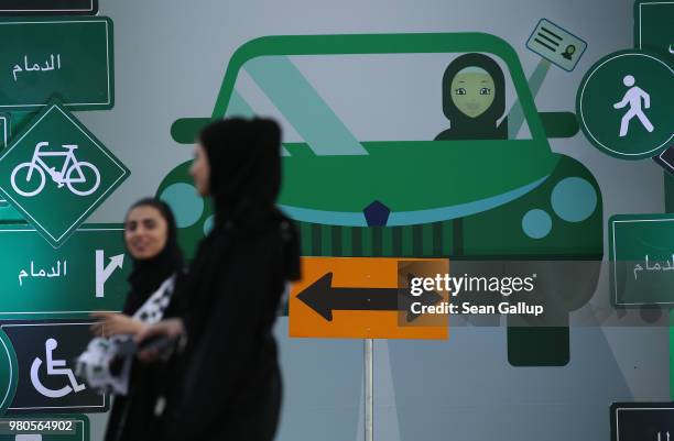 Young women wearing the traditional abaya walk past a sign as they help to organize an outdoor educational driving event for women on June 21, 2018...