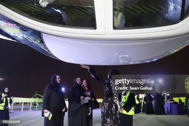 Guide explains the importance of safety belts at a car that is suspended upside down to a group of women at an outdoor educational driving event for...