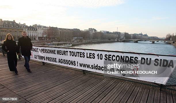 Un couple passe, le 29 novembre 2008 sur le pont des Arts à Paris, devant une banderole déployée par l'association Sidaction à l'occasion de la...