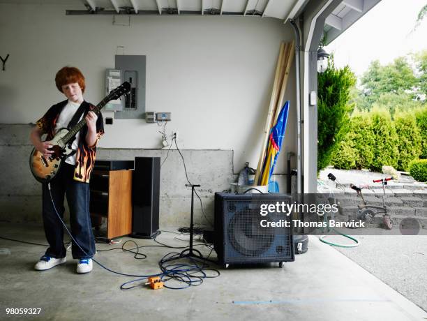 young male standing in garage playing guitar - electric guitar stock-fotos und bilder