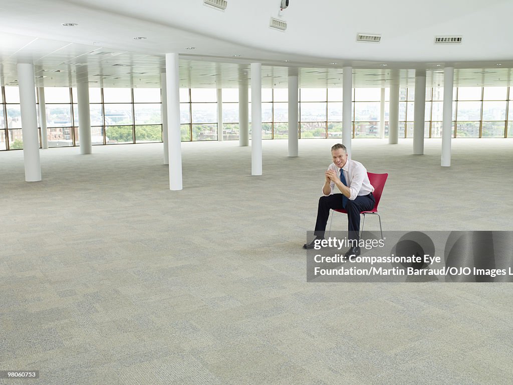 Smiling man sitting on red chair in large room