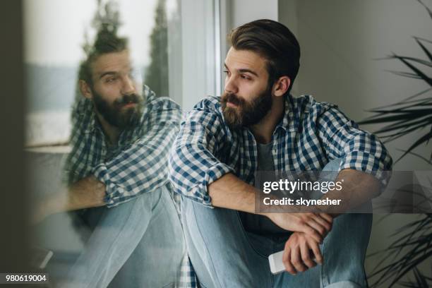 nadenkende man ontspannen op vensterbank thuis. - lonely man stockfoto's en -beelden