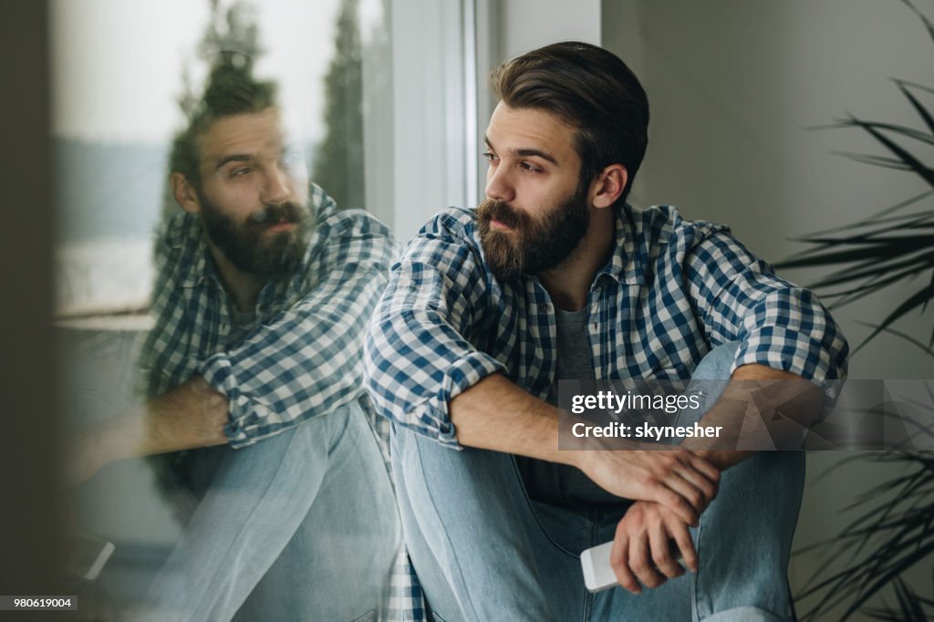 Thoughtful man relaxing on window sill at home.