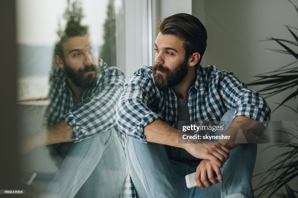 Homem pensativo relaxando no peitoril da janela em casa.