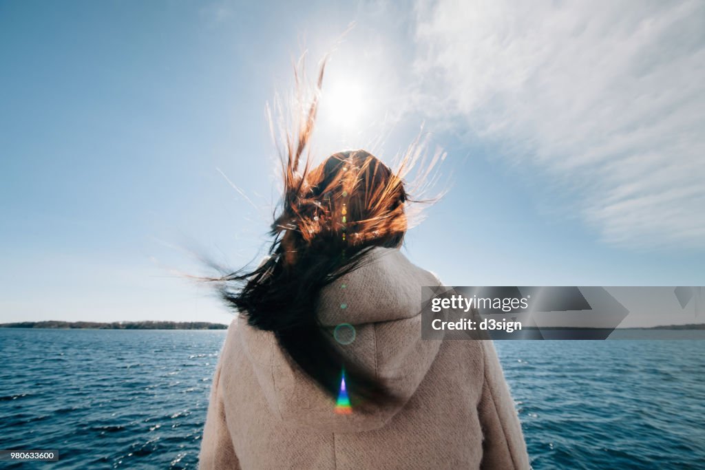 Rear view of woman standing on boat enjoying sea breeze and admiring ocean