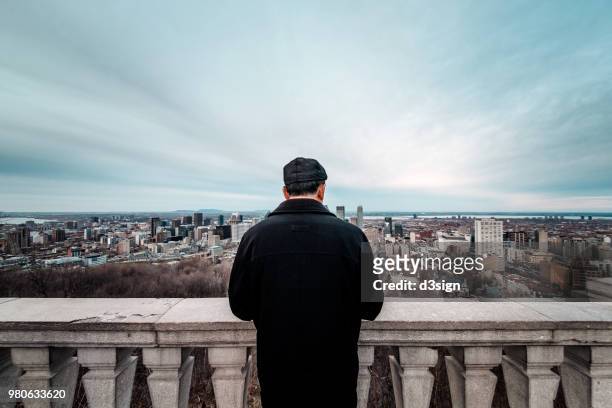 rear view of man admiring city skyline of montreal from balcony - montréal stock-fotos und bilder