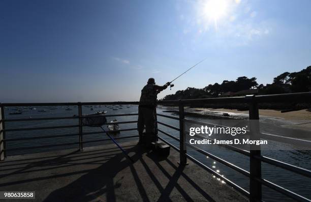 Man fishing on a jetty as the sun begins to set on the longest day in the Northern Hemisphere on June 21, 2018 in Arcachon Bay, France. Situated only...