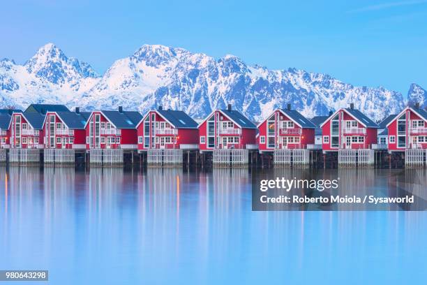 traditional wood houses called rorbu in the fishing village of svolvaer surrounded by cold sea and snowcapped mountains at dusk, lofoten islands, norway - svolvaer stock pictures, royalty-free photos & images