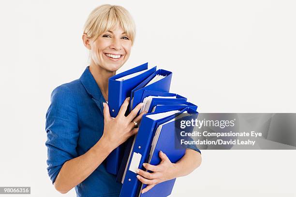 smiling woman holding a stack of blue binders - binders stockfoto's en -beelden