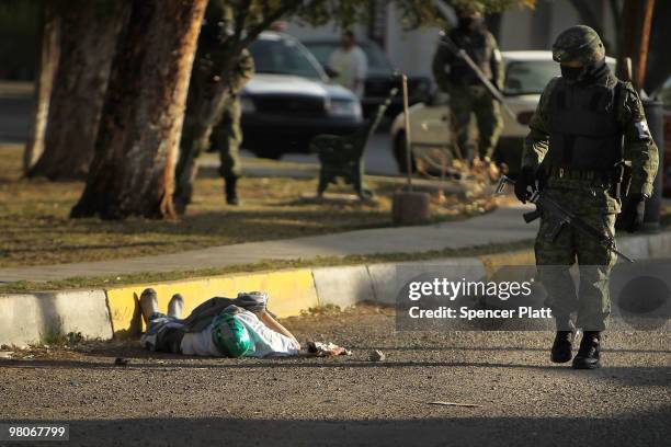 Member of the military police walks by a body with a mask in the street, one of numerous murders over a 24 hour period, on March 26, 2010 in Juarez,...