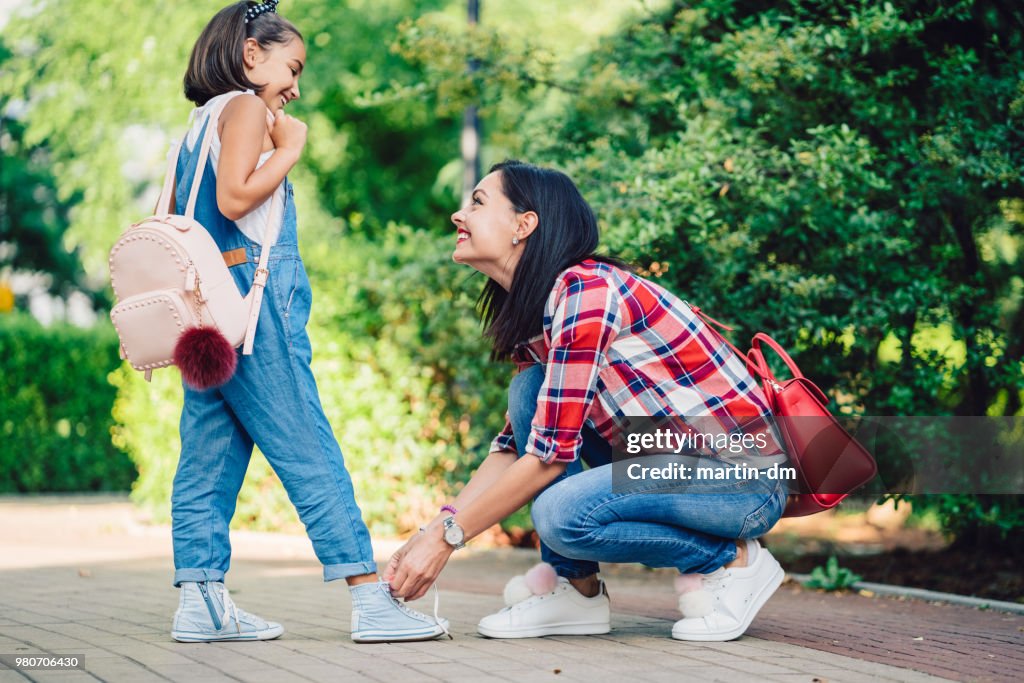 Smiling mother tying shoelaces of her daughter in the park