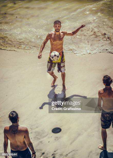 three young brazilian men playing soccer on copacabana beach on a hot summer day in rio de janeiro, brazil - grafissimo stock pictures, royalty-free photos & images