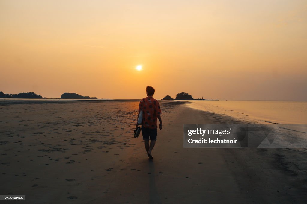 Young man relaxing by the ocean, watching the sunset on the beautiful island of Koh Lanta, Thailand
