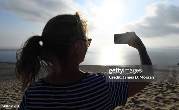 Woman takes a photo on her mobile phone on top of the Dune Du Pilat as the sun begins to set on the longest day in the Northern Hemisphere on June...