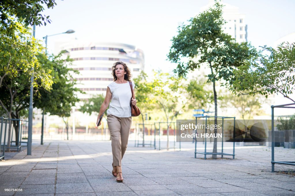 Mature businesswoman walking on footpath in city