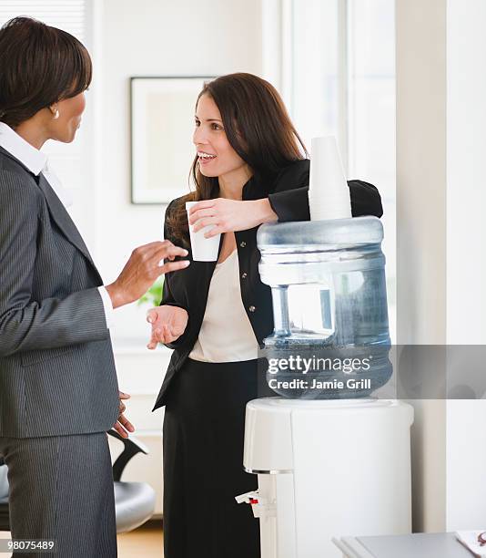 businesswomen talking by water cooler - trinkwasserbehälter stock-fotos und bilder