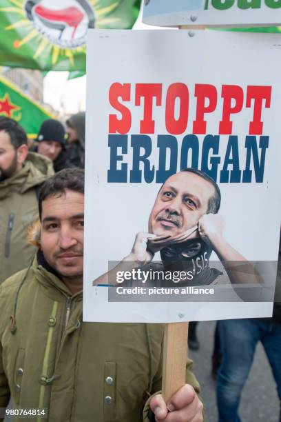 March 2018, Germany, Munich: A protestor holding up a sign with an image of the Turkish president Erdogan and the inscription "stop Erdogan" in order...