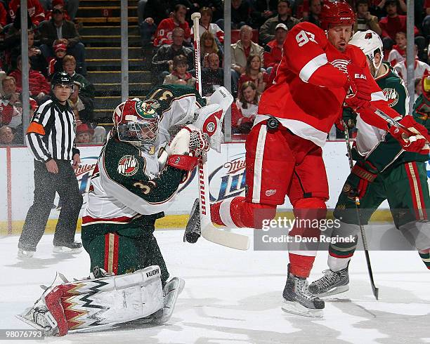 Johan Franzen of the Detroit Red Wings get knocked into Nick Schultz of the Minnesota Wild as teammate Josh Harding gets ready to make a glove save...