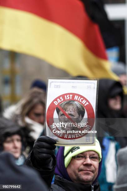 March 2018, Germany, Cottbus: A participant in the anti-refugee demonstration by the group "Zukunft Heimat" holds a sign featuring German Chancellor...