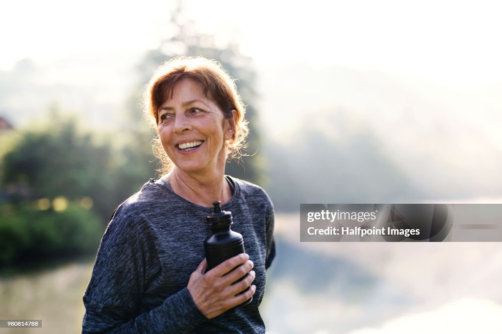 Senior woman resting after exercise outdoors in nature in the foggy morning. Copy space.