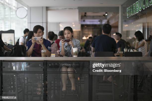 Customers use smartphones while sitting in a Starbucks Corp. Coffee shop at the CentralWorld shopping mall, operated by Central Pattana Pcl , in...